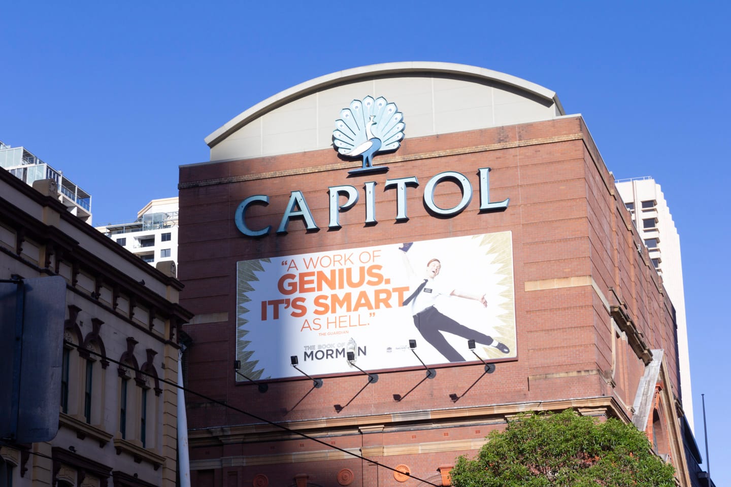 The iconic Capitol peacock and wordmark on the west facing wall of the building. Below it is a billboard for musical “The Book of Mormon”.