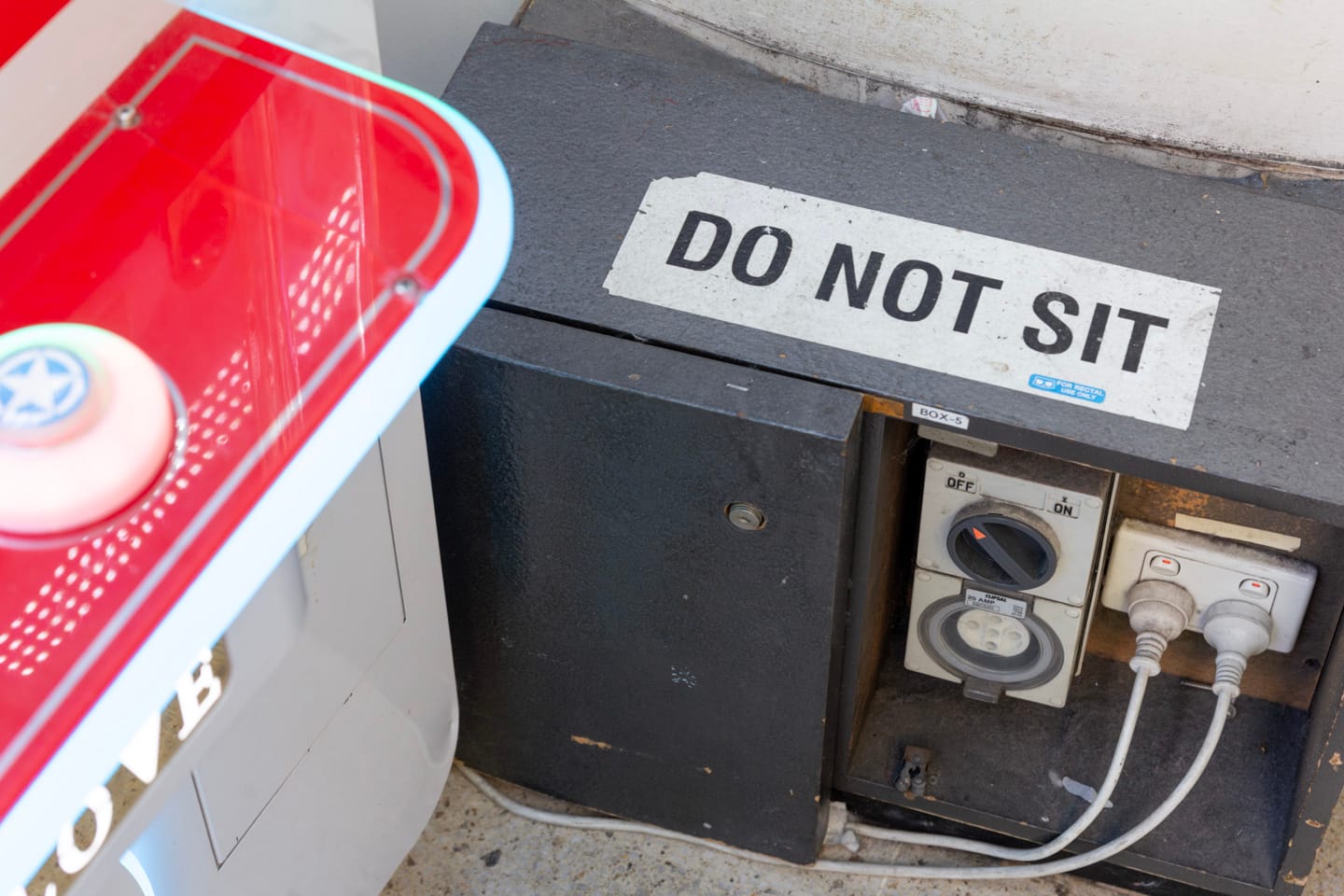 A lockbox with a three-phase power port and regular AC port. Above it has a label “DO NOT SIT”, and affixed on top a tiny sticker labelled “FOR RECTAL USE ONLY”.